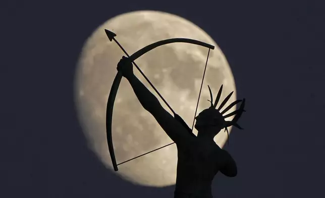 The bronze sculpture of "Ad Astra" a Kansa Indian, perched atop the Kansas State Capitol dome is silhouetted against the waxing moon, Monday, Oct. 14, 2024, in Topeka, Kan. (AP Photo/Charlie Riedel)