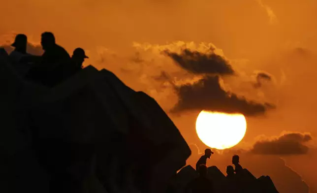 Displaced men fleeing the Israeli airstrikes in Beirut's Dahiyeh suburb, sit at Beirut's seaside promenade, along the Mediterranean Sea while the sun sets over the capital Beirut, Lebanon, Thursday, Oct. 17, 2024. (AP Photo/Hassan Ammar)