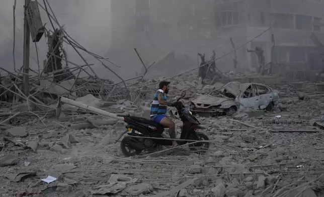 A man rides his scooter as he drives on the debris of destroyed buildings that were hit by Israeli airstrikes in Dahiyeh, Beirut, Lebanon, Sunday, Oct. 6, 2024. (AP Photo/Hussein Malla)