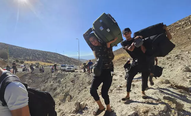 Syrians carry their luggage as they cross on foot into Syria through a crater caused by an Israeli airstrike to cut the road between the Lebanese and the Syrian checkpoints, at the Masnaa crossing, in the eastern Bekaa Valley, Lebanon, Friday, Oct. 4, 2024. (AP Photo/Samer Husseini)