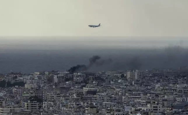 A Middle East Airlines airplane flies over Beirut as smoke rises from Dahiyeh, in Beirut, Lebanon, Tuesday, Oct. 1, 2024. (AP Photo/Bilal Hussein)