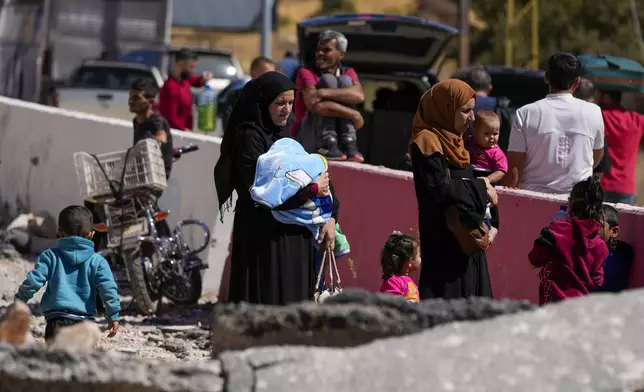 People carry their luggage as they cross into Syria on foot, through a crater caused by Israeli airstrikes aiming to block Beirut-Damascus highway at the Masnaa crossing, in the eastern Bekaa Valley, Lebanon, Saturday, Oct. 5, 2024. (AP Photo/Hassan Ammar)