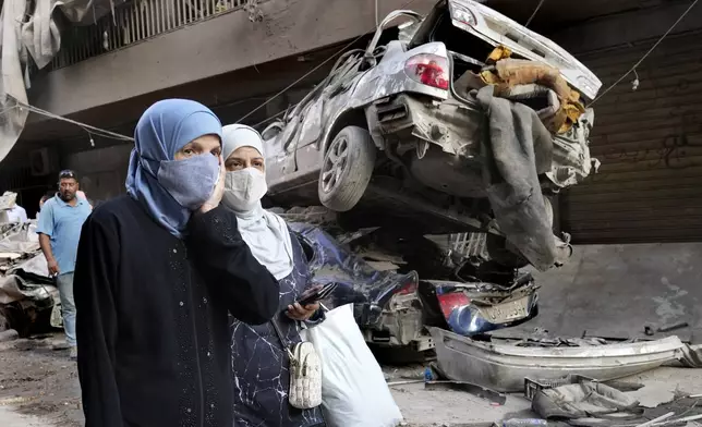 Lebanese women pass near destroyed cars, at the site of Thursday's Israeli airstrike, in Beirut, Lebanon, Friday, Oct. 11, 2024. (AP Photo/Hussein Malla)