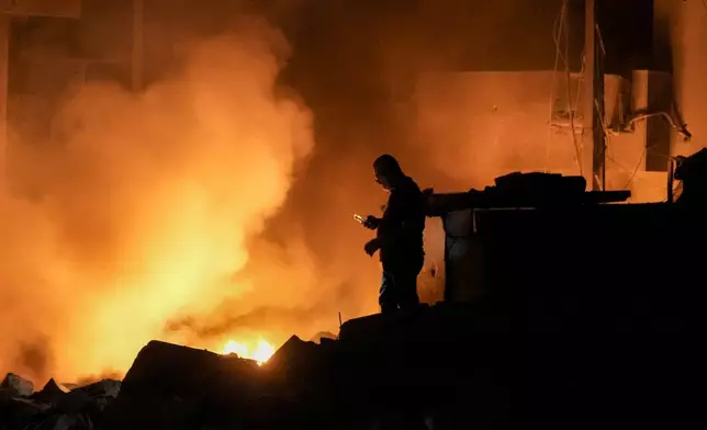 A man uses his mobile phone as flames and smoke rise at the scene of buildings hit by an Israeli airstrike in central Beirut, Lebanon, Thursday, Oct. 10, 2024. (AP Photo/Bilal Hussein)