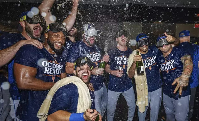 The New York Mets celebrate in the locker room after clinching a playoff berth with a victory in the first baseball game of a doubleheader against the Atlanta Braves, Monday, Sept. 30, 2024, in Atlanta. (AP Photo/Jason Allen)