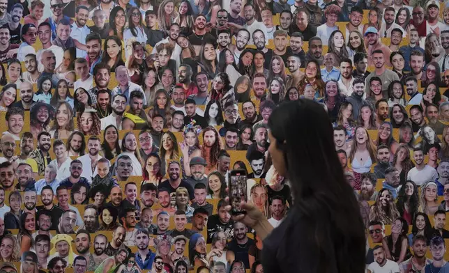 An attendant walks through a mural with portraits of the victims at the site of the Nova music festival, where hundreds of revelers were killed and abducted by Hamas and taken into Gaza, on the one-year anniversary of the attack, near Kibbutz Reim, southern Israel, Monday, Oct. 7, 2024. (AP Photo/Ariel Schalit)