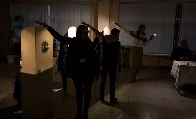 Election officials assist voters with mobile phone flashlights during a power failure in Chisinau, Moldova, Sunday, Oct. 20, 2024, during a presidential election and a referendum on whether to enshrine in the Constitution the country's path to European Union membership. (AP Photo/Nicolae Dumitrache)