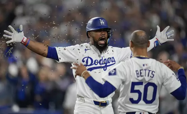 Los Angeles Dodgers' Teoscar Hernández, left, gets sunflower seeds to the face to celebrate his solo home run as Mookie Betts (50) looks on during the seventh inning in Game 5 of a baseball NL Division Series against the San Diego Padres, Friday, Oct. 11, 2024, in Los Angeles. (AP Photo/Ashley Landis)