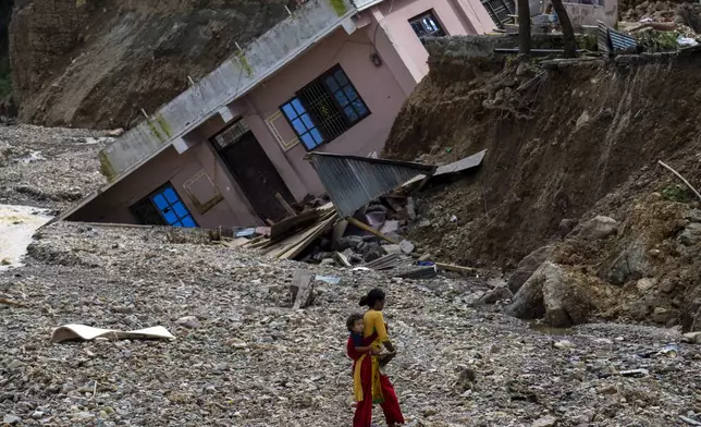 A woman with a child on her back walks past a house which had collapsed due to flooding in the Nakhu river caused by heavy rains in Lalitpur, Nepal, on Tuesday, Oct. 1, 2024. (AP Photo/Niranjan Shrestha)