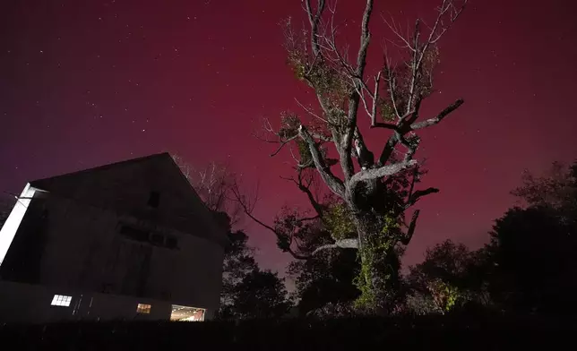 An aurora borealis, also known as the northern lights, glows red in the sky above a barn, Thursday, Oct. 10, 2024, in East Derry, N.H. (AP Photo/Charles Krupa)