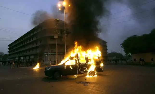 Police and paramilitary soldiers stand beside a police vehicle setting on fire by supporters of the Tehreek-e-Labbaik Pakistan party during clashes in Karachi, Pakistan, Sunday, Oct. 13, 2024. (AP Photo/Fareed Khan)