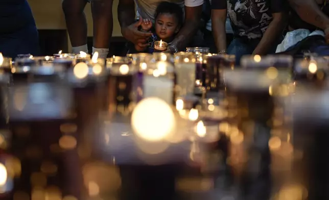 Reinaldo Almanza holds his son Reinier with a candle at San Felipe Church in honor of the Black Christ in Portobelo, Panama, Monday, Oct. 21, 2024, during a festival celebrating the iconic statue that was found on the shore in 1658. (AP Photo/Matias Delacroix)