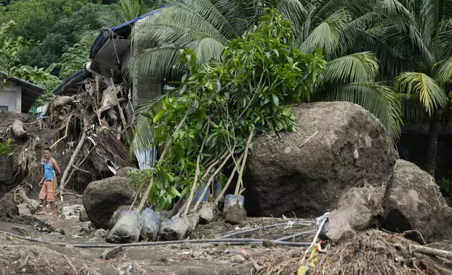 A resident passes by large boulders beside damaged homes on Saturday, Oct. 26, 2024 after being struck by a landslide triggered by Tropical Storm Trami in Talisay, Batangas province, Philippines. (AP Photo/Aaron Favila)