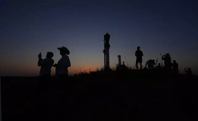 People take photos as the sun sets behind SpaceX's mega rocket Starship, Saturday, Oct. 12, 2024, in Boca Chica, Texas. (AP Photo/Eric Gay)