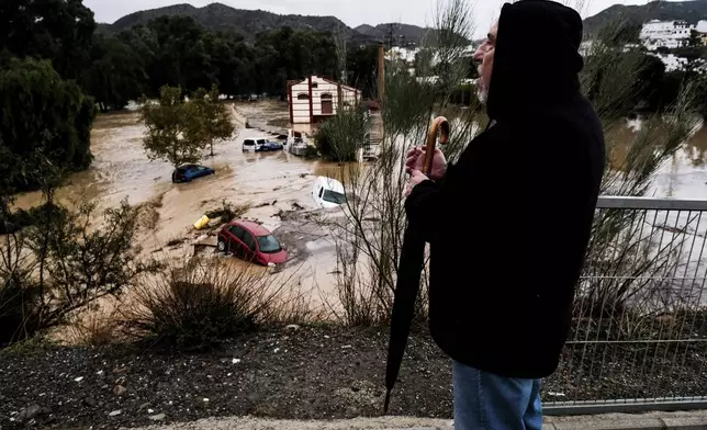 A man observes several cars being swept away by the water, after floods preceded by heavy rains caused the river to overflow its banks in the town of Alora, Malaga, Spain, Tuesday, Oct. 29, 2024. (AP Photo/Gregorio Marrero)