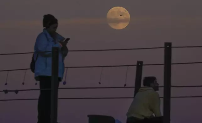 An airplane crosses the supermoon as people watch it rise over Lake Michigan, Wednesday, Oct. 16, 2024, in Chicago. (AP Photo/Erin Hooley)