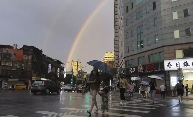 People walk in the rain with a backdrop of the rainbow in the sky as Typhoon Krathon approaches to Taiwan in Taipei, Monday, Sept. 30, 2024. (AP Photo/Chiang Ying-ying)