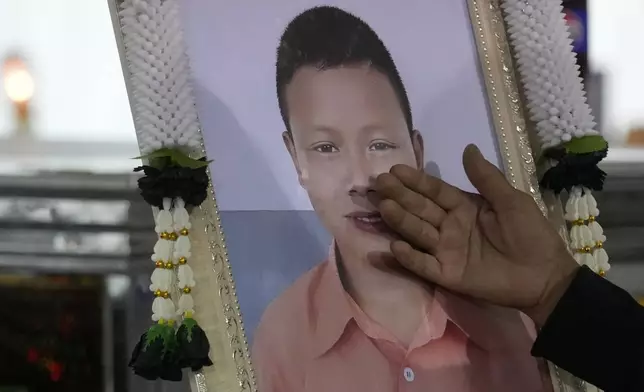 A relative touches a portrait of a victim of a school bus fire at Wat Khao Phraya Sangkharam School Lan Sak, Uthai Thani province, Thailand, Thursday, Oct. 3, 2024. (AP Photo/Sakchai Lalit)