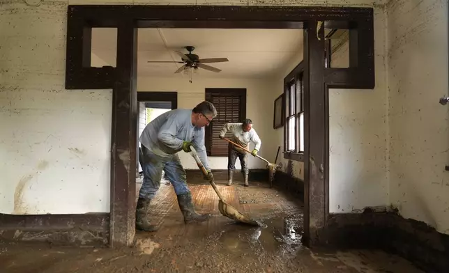 Ben Phillips, left, and his wife Becca Phillips scrape mud out of the living room of their home left in the wake of Hurricane Helene, Tuesday, Oct. 1, 2024, in Marshall, N.C. (AP Photo/Jeff Roberson)