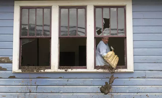 Ben Phillips scoops mud out a window of his house left in the wake of Hurricane Helene, Tuesday, Oct. 1, 2024, in Marshall, N.C. (AP Photo/Jeff Roberson)