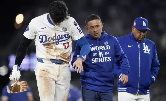 Los Angeles Dodgers' Shohei Ohtani is helped off the field after getting hurt during the seventh inning in Game 2 of the baseball World Series against the New York Yankees, Saturday, Oct. 26, 2024, in Los Angeles. (AP Photo/Ashley Landis)