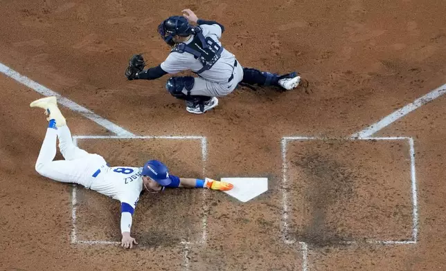 Los Angeles Dodgers' Kiké Hernández, bottom, scores past New York Yankees catcher Austin Wells on a sacrifice fly ball by Will Smith during the fifth inning in Game 1 of the baseball World Series, Friday, Oct. 25, 2024, in Los Angeles. (AP Photo/Mark J. Terrill)