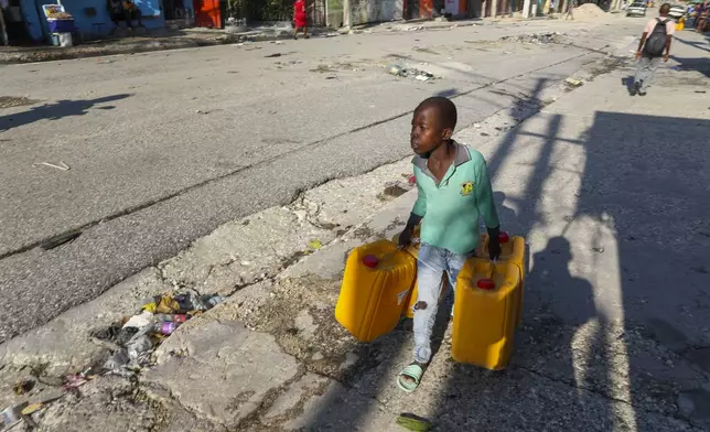 A youth carries empty containers as fetches drinking water in Port-au-Prince, Haiti, Tuesday, Oct. 1, 2024. (AP Photo/Odelyn Joseph)