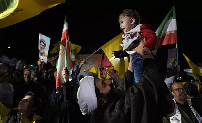 A cleric holds up his son as he celebrates Iran's missile strike against Israel during an anti-Israeli protest at Felestin (Palestine) Square in Tehran, Iran, Tuesday, Oct. 1, 2024. (AP Photo/Vahid Salemi)