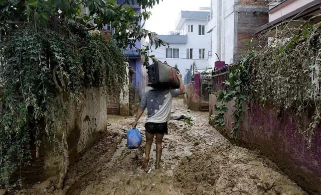 A man walks on a muddy alleyway carrying belongings salvaged from his house in Kathmandu, Nepal, Monday, Sept. 30, 2024 in the aftermath of a flood caused by heavy rains. (AP Photo/Gopen Rai)