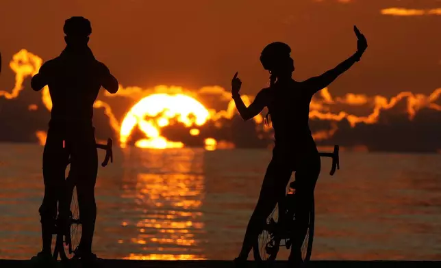 A pair of cyclists take photos as the sun rises over the Atlantic Ocean, Thursday, Oct. 3, 2024, in Bal Harbour, Fla. (AP Photo/Wilfredo Lee)