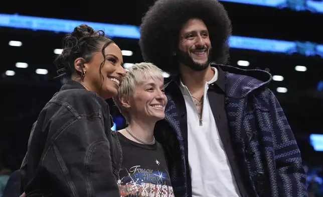 Megan Rapinoe, center, Colin Kaepernick, right, and Nessa Diab, left, pose for photographs during the second half of a WNBA basketball semifinal game between the New York Liberty and the Las Vegas Aces, Tuesday, Oct. 1, 2024, in New York. The Liberty won 88-84. (AP Photo/Frank Franklin II)