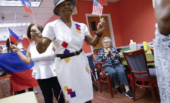 A woman from Haiti holds flags during a multicultural parade at Sunshine Adult Day Center in Bergenfield, N.J., Monday, Aug. 26, 2024. (AP Photo/Kena Betancur)