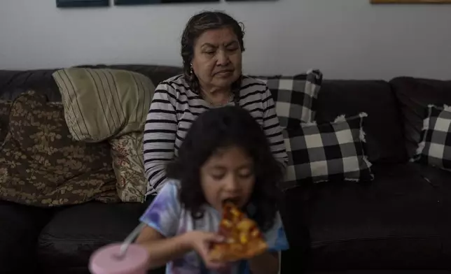 Marina Maalouf, a longtime resident of Hillside Villa, sits on a sofa as her granddaughter eats pizza for lunch in their apartment in Los Angeles, Tuesday, Oct. 1, 2024. (AP Photo/Jae C. Hong)