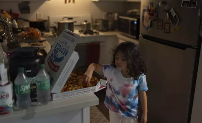 Rubie Caceres, a granddaughter of Marina Maalouf, a longtime resident of Hillside Villa, grabs a slice of pizza in her apartment in Los Angeles, Tuesday, Oct. 1, 2024. (AP Photo/Jae C. Hong)