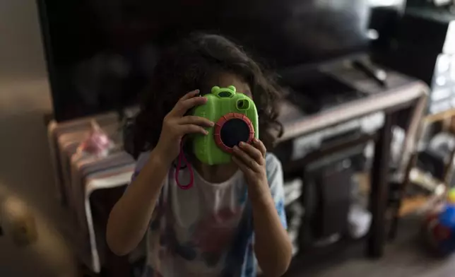 Rubie Caceres, a granddaughter of Marina Maalouf, a longtime resident of Hillside Villa, plays with a toy camera in her apartment in Los Angeles, Tuesday, Oct. 1, 2024. (AP Photo/Jae C. Hong)