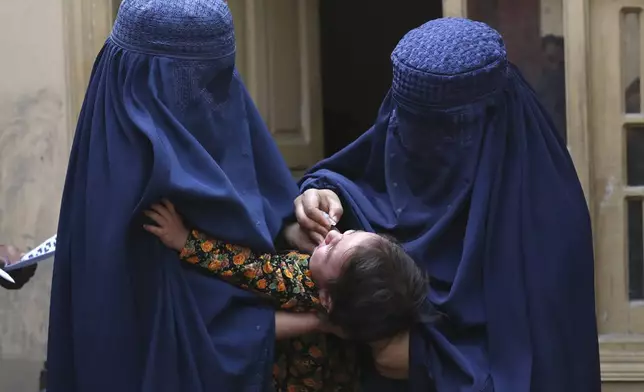 A health worker, right, administers a polio vaccine to a child at a neighborhood of Jalalabad, east of Kabul, Afghanistan, Tuesday, Oct. 29, 2024. (AP Photo/Shafiullah Kakar)