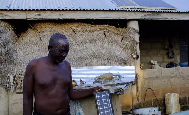 Yakubu Achiri holds a solar panel that he uses to power his light bulb at his house in Gushegu northern, Ghana, Friday Sept. 6, 2024. (AP Photos/Abdul Haqq Mahama)