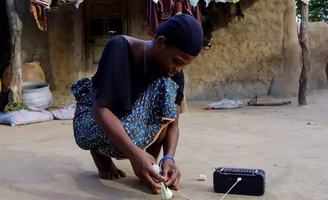 Rukaya Tongdoo connects a torchlight to a solar powered radio outside her house in Gushegu northern, Ghana, Friday Sept 6, 2024. (AP Photos/Abdul Haqq Mahama)