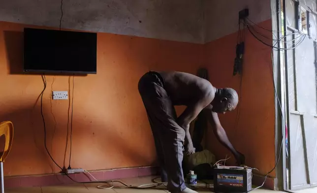 Yakubu Achiri fixes a car battery to his solar system at his house in Gushegu northern, Ghana, Friday Sept. 6, 2024. (AP Photos/Abdul Haqq Mahama)