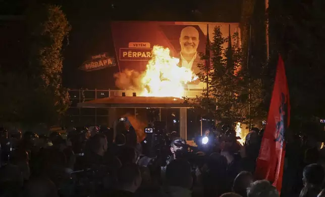 Fire burns behind a riot police cordon and in front of a poster depicting the Albania Prime minister Edi Rama during an anti-government rally set up by the opposition, in Tirana, Albania, Monday, Oct. 7, 2024. (AP Photo/Hameraldi Agolli)