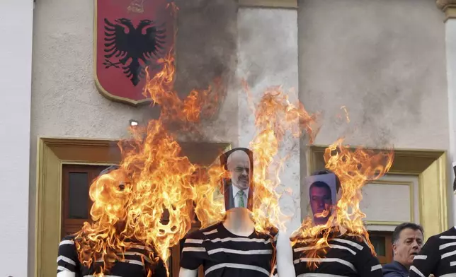 Albanian opposition lawmakers put fire on mannequins depicting members of the Socialist Party government, with a photo of Prime Minister Edu Rama in the center, during a protest for the imprisonment of a fellow lawmaker in Tirana, Albania, Thursday, Oct. 3, 2024. (AP Photo/Hameraldi Agolli)