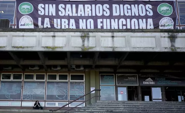 A student sits on the steps of the University of Buenos Aires (UBA) under a banner that reads in Spanish, "Without decent wages, UBA doesn't work," protesting President Javier Milei's veto of a law to increase funding for public universities in Buenos Aires, Argentina, Wednesday, Oct. 16, 2024. (AP Photo/Natacha Pisarenko)