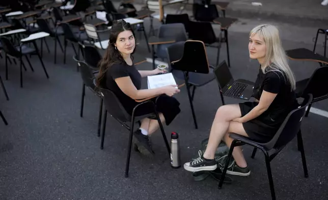 Students Antonia Goycochea, left, and Iana Ferrari sit in the middle of a street outside the Faculty of Psychology during a protest against President Javier Milei's veto of higher funding for public universities, in Buenos Aires, Argentina, Wednesday, Oct. 16, 2024. (AP Photo/Natacha Pisarenko)