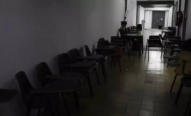 A student sits inside an empty hallway inside the Faculty of Psychology as fellow students hold class outside in the middle of a street to protest President Javier Milei's veto of higher funding for public universities, in Buenos Aires, Argentina, Wednesday, Oct. 16, 2024. (AP Photo/Natacha Pisarenko)