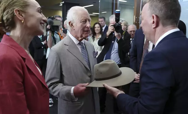 Britain's King Charles III, center, receives a bush hat as a gift from co-medical directors Georgina Long, left, and Richard Scoyler, right, during his visit to the Melanoma Institute of Australia on Tuesday Oct. 22, 2024 in Sydney, Australia. (David Gray/Pool Photo via AP)