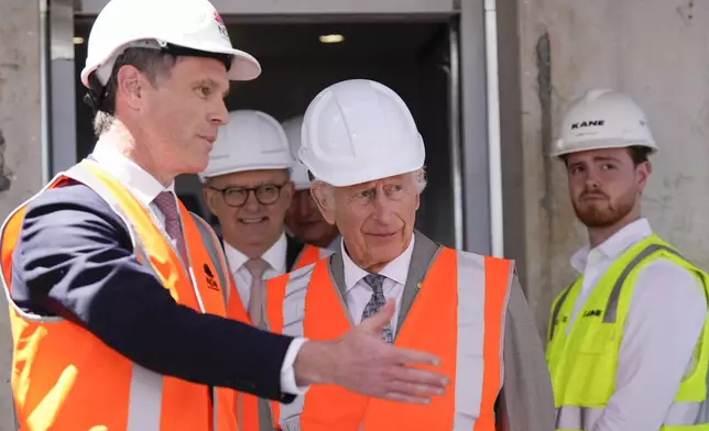 Britain's King Charles III, center, is assisted by New South Wales Premier Chris Minns, left, while Australia's Prime Minister Anthony Albanese walks behind during his visit at the Homes NSW Cowper Street development in Sydney, Australia, Tuesday, Oct. 22, 2024. (AP Photo/Mark Baker, Pool)