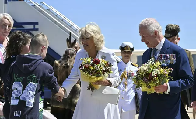 Britain's King Charles III, right, and Queen Camilla, center, receive flowers after arriving at Defense Establishment Fairbairn in Canberra, Australia, Monday, Oct. 21, 2024. (Saeed Khan/Pool Photo via AP)