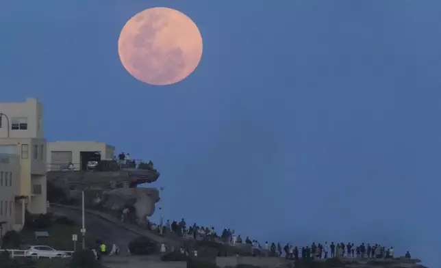 People watch from a cliff top as the moon rises at Bondi Beach in Sydney, Australia, Thursday, Oct. 17, 2024. (AP Photo/Mark Baker)