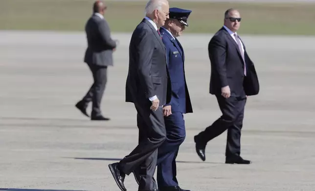 President Joe Biden, center left, is escorted by Col. Paul Pawluk, Vice Commander, 89th Airlift Wing, center right, as he walks from Marine One before boarding Air Force One at Joint Base Andrews, Md., Tuesday, Oct. 22, 2024. (AP Photo/Luis M. Alvarez)