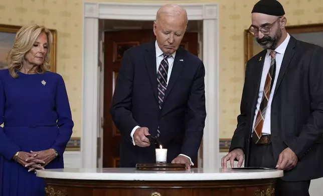 President Joe Biden, center, standing with first lady Jill Biden, left, and Rabbi Aaron Alexander of the Adas Israel Congregation, lights a memorial candle in the Blue Room of the White House in Washington, Monday, Oct. 7, 2024, to mark the one-year anniversary of the Hamas attack on Israel that left about 1,200 people dead. (AP Photo/Susan Walsh)